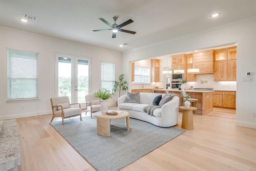 Living area with built in adjustable shelves, light engineered wood flooring, a stone fireplace with solid cedar mantle, ceiling fan, and french doors that open to a covered back patio.