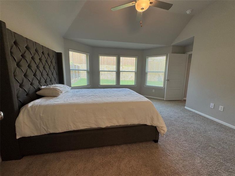 Spacious room featuring a vaulted ceiling with a ceiling fan, a bay window with blinds, and soft carpet flooring Spacious room featuring a vaulted ceiling with a ceiling fan, a bay window with blinds, and soft carpet flooring