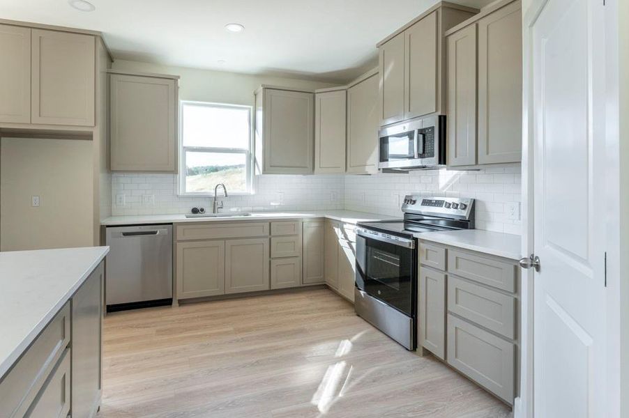 Kitchen featuring gray cabinets, stainless steel appliances, tasteful backsplash, light wood-type flooring, and light stone countertops