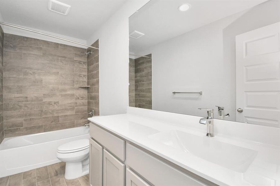 Indulge in refined charm in the secondary bathroom, where the tile flooring harmonizes with a bath/shower combo surrounded by tasteful tile. Light wood cabinets, coupled with a gorgeous countertop, elevate the space, cultivating a truly welcoming atmosphere. Sample photo of completed home with similar floor plan. Actual colors and selections may vary.