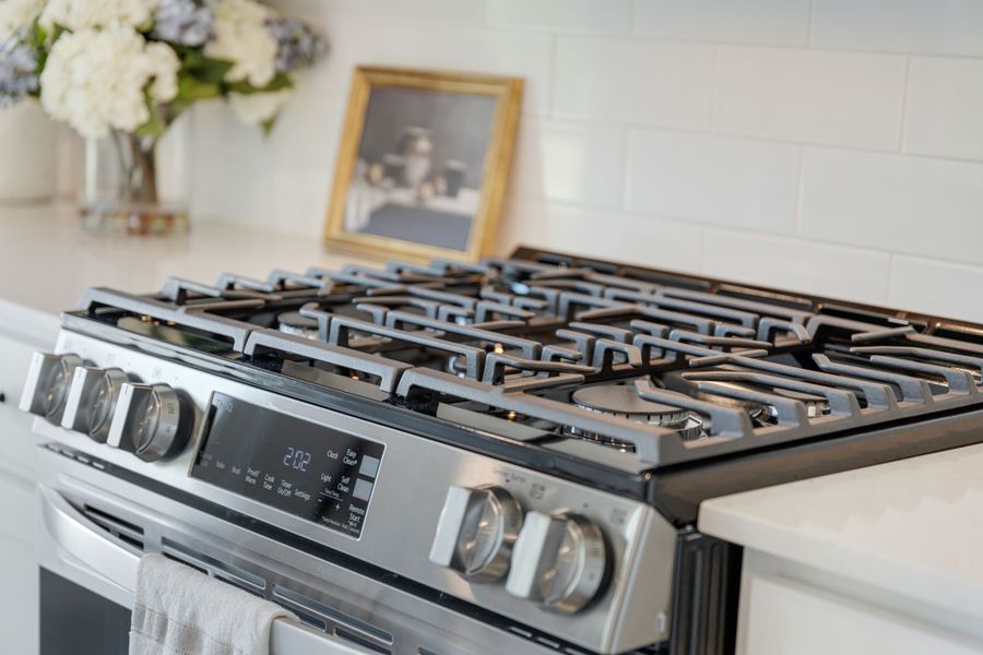 A stove top with a vase of flowers on the side. A stove top with a vase of flowers on the side.