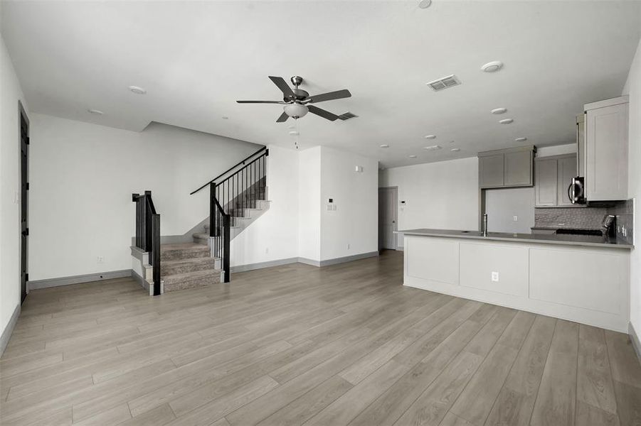 Unfurnished living room with stairs, light wood-style floors, a ceiling fan, and recessed lighting Unfurnished living room with stairs, light wood-style floors, a ceiling fan, and recessed lighting