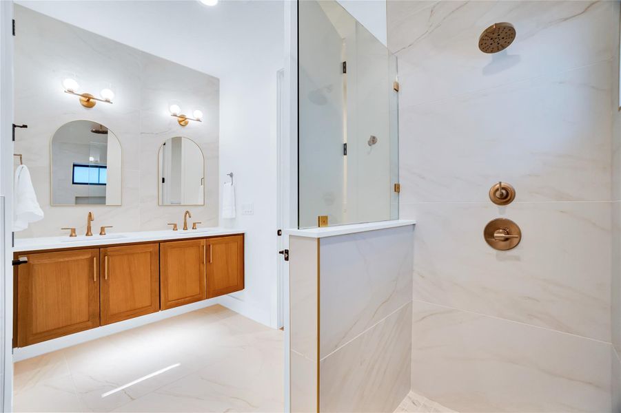 Bathroom featuring double vanity, walk in shower, and light marble finish floors Bathroom featuring double vanity, walk in shower, and light marble finish floors