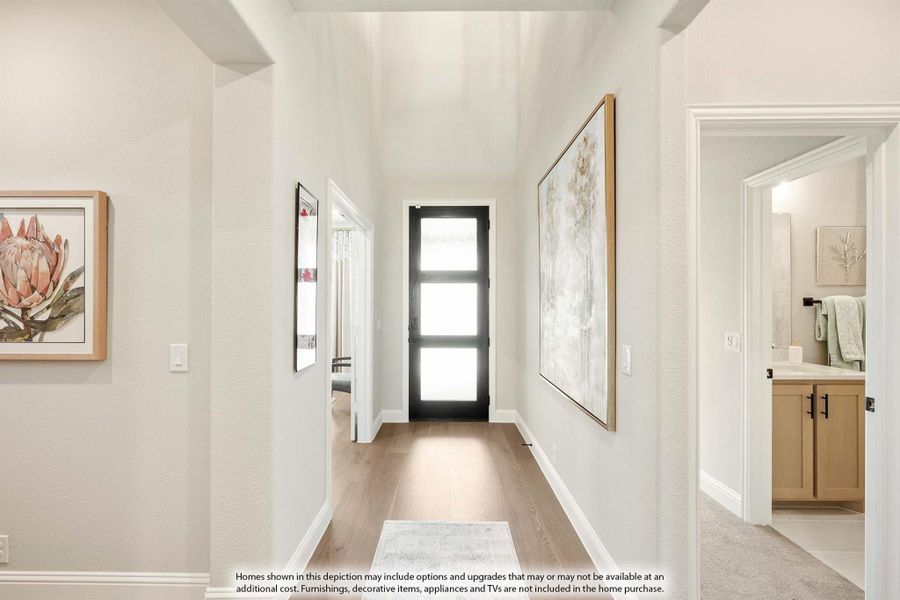 Hallway with light wood floors, black glass-panel door, framed wall art, and bathroom entrance visible on the right.