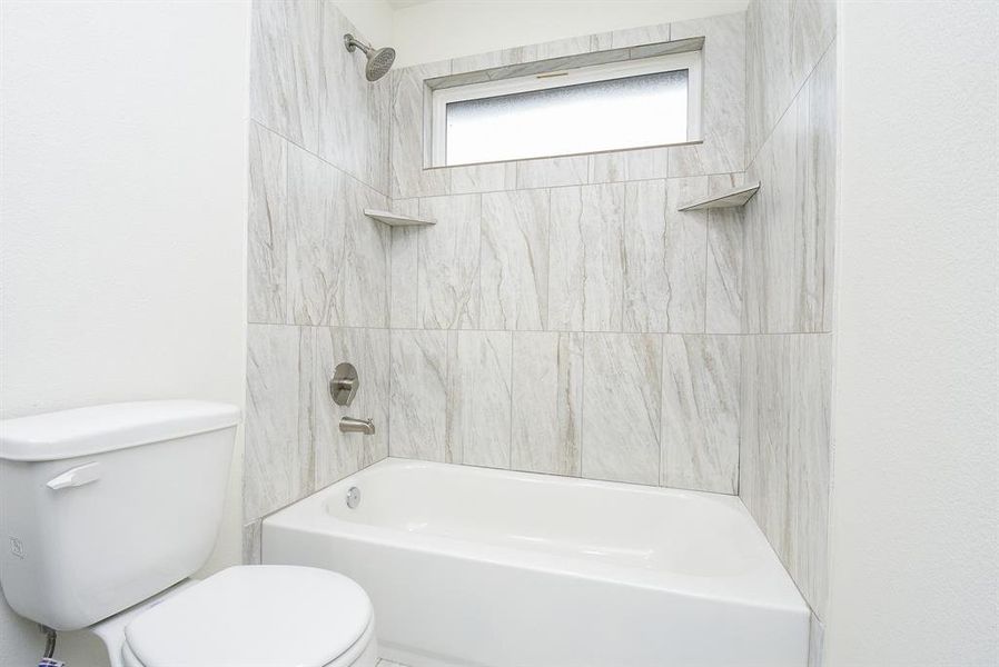 A modern bathroom with tiles featuring a toilet and a bathtub with a built-in shower and a small window.