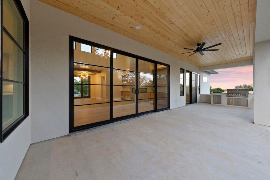 An inviting outdoor living space features expansive glass doors, a wooden ceiling, and a built-in barbecue area.