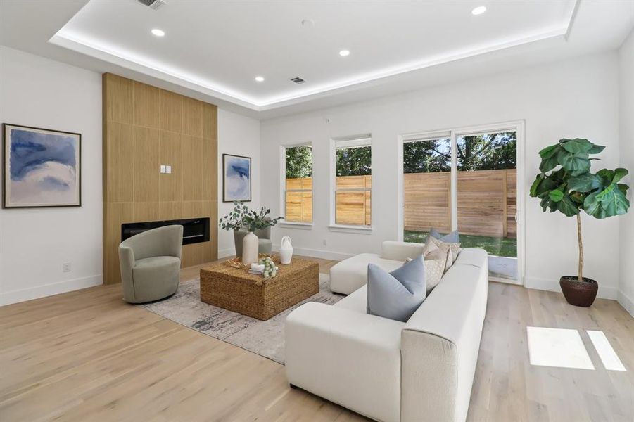 Living area with recessed lighting, a raised ceiling, light wood-style floors, and a large fireplace