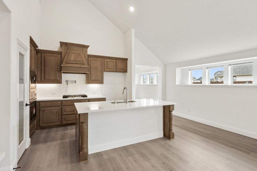 Kitchen with brown wood cabinets, white island with sink, and vaulted ceiling open to dining area Kitchen with brown wood cabinets, white island with sink, and vaulted ceiling open to dining area