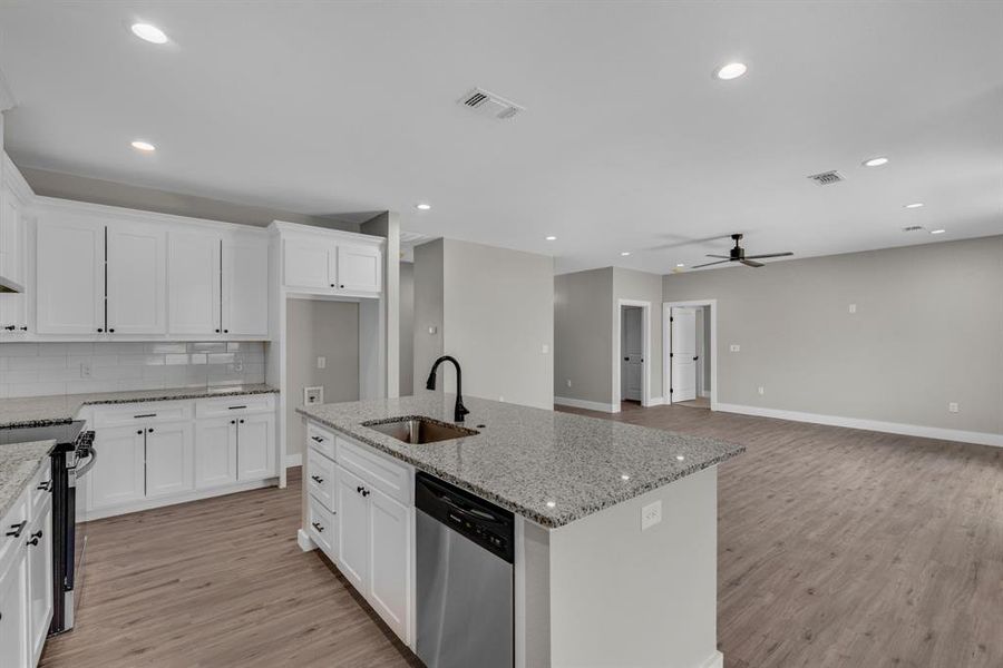 Kitchen with light stone countertops, appliances with stainless steel finishes, a kitchen island with sink, sink, and ceiling fan