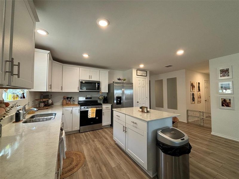 Kitchen with white cabinets, appliances with stainless steel finishes, dark wood finished floors, recessed lighting, and light stone countertops