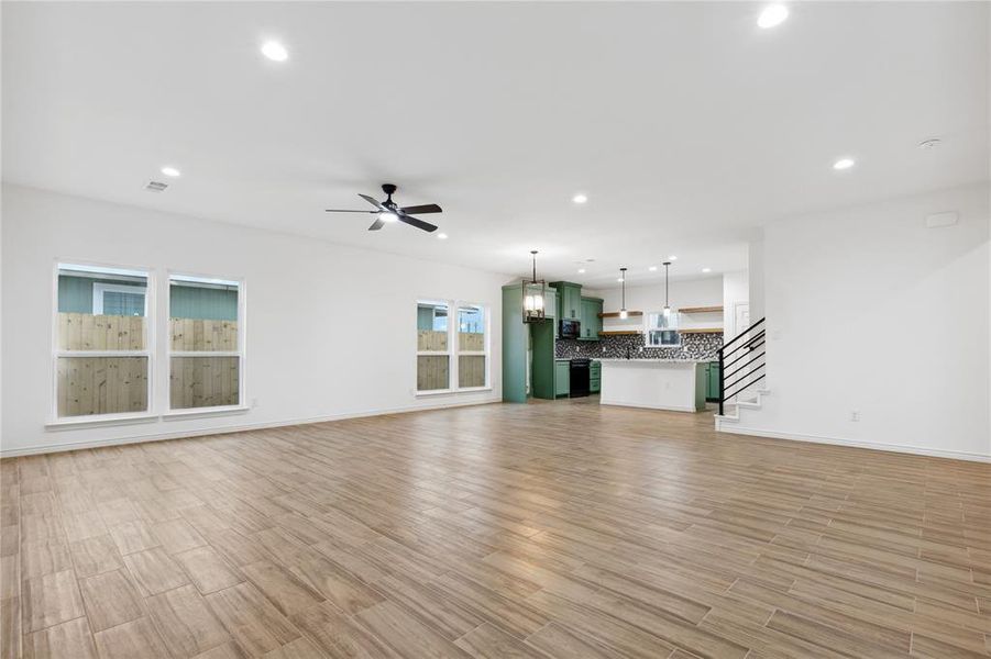 Unfurnished living room with ceiling fan with notable chandelier and light hardwood / wood-style flooring