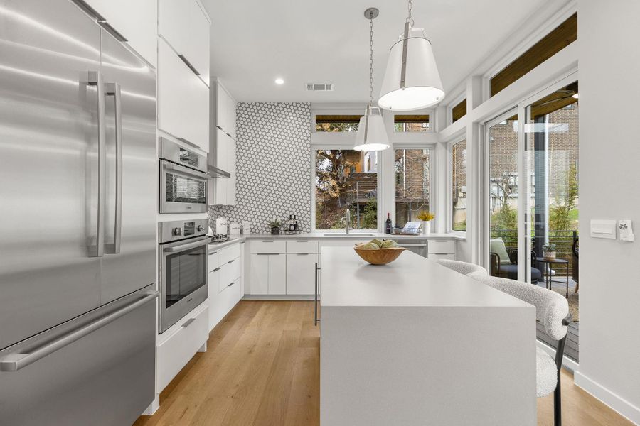 Kitchen featuring built in fridge, a center island, pendant lighting, white cabinetry, and modern cabinets