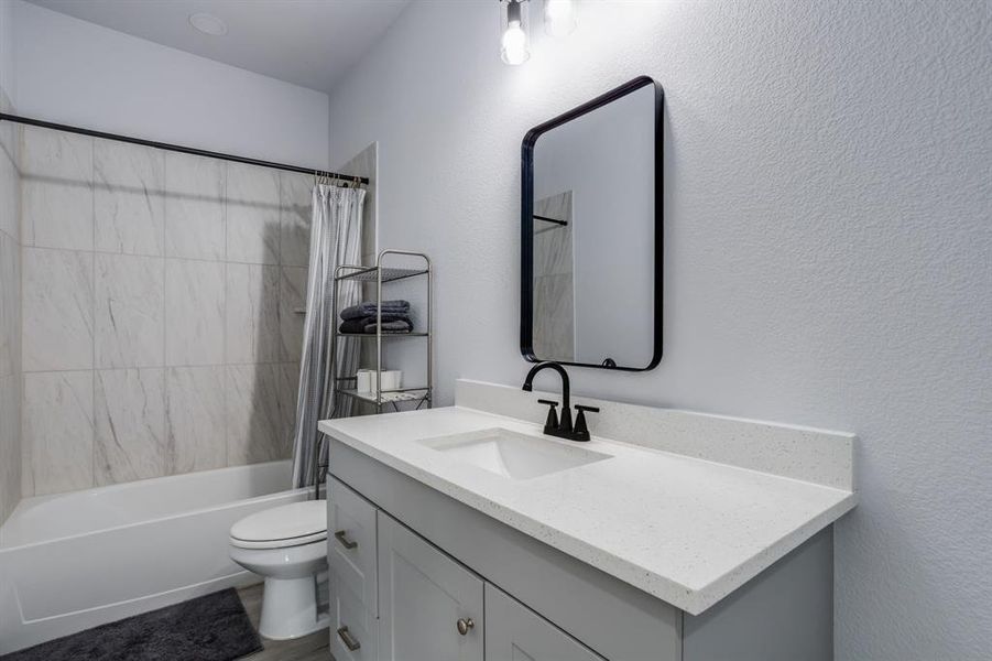 Full bath with shower / tub combo with curtain, vanity, and a textured wall Full bath with shower / tub combo with curtain, vanity, and a textured wall