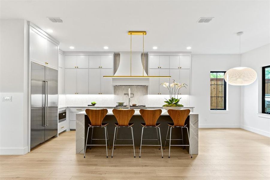 Kitchen featuring built in refrigerator, custom range hood, a center island with sink, recessed lighting, and light countertops