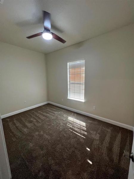 Empty room featuring dark colored carpet and ceiling fan