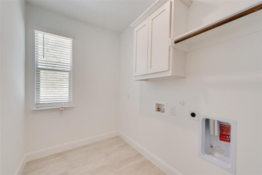 Washroom with cabinets, light tile patterned floors, washer hookup, and a wealth of natural light