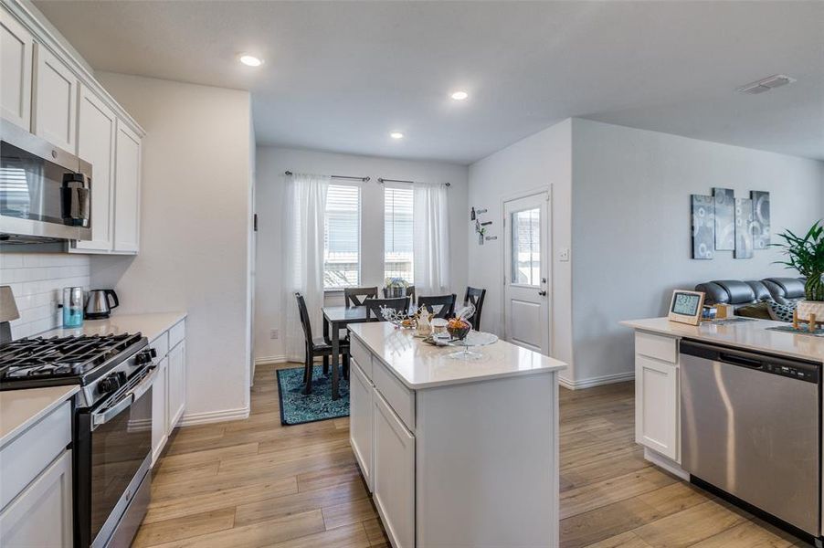 Kitchen featuring appliances with stainless steel finishes, light wood-type flooring, backsplash, white cabinets, and a center island