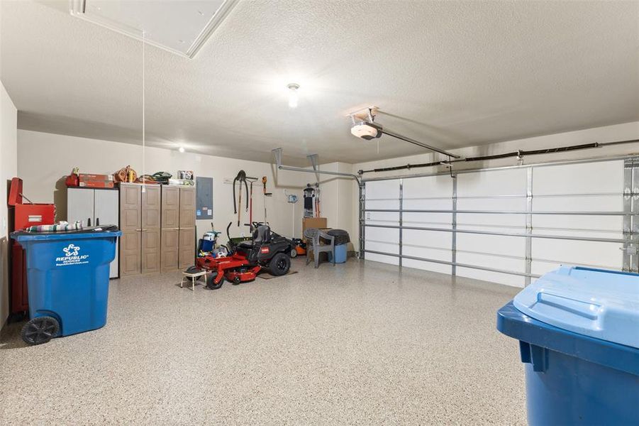 Spacious garage featuring a light-toned epoxy floor coating, two overhead garage doors, and an attic access panel Spacious garage featuring a light-toned epoxy floor coating, two overhead garage doors, and an attic access panel