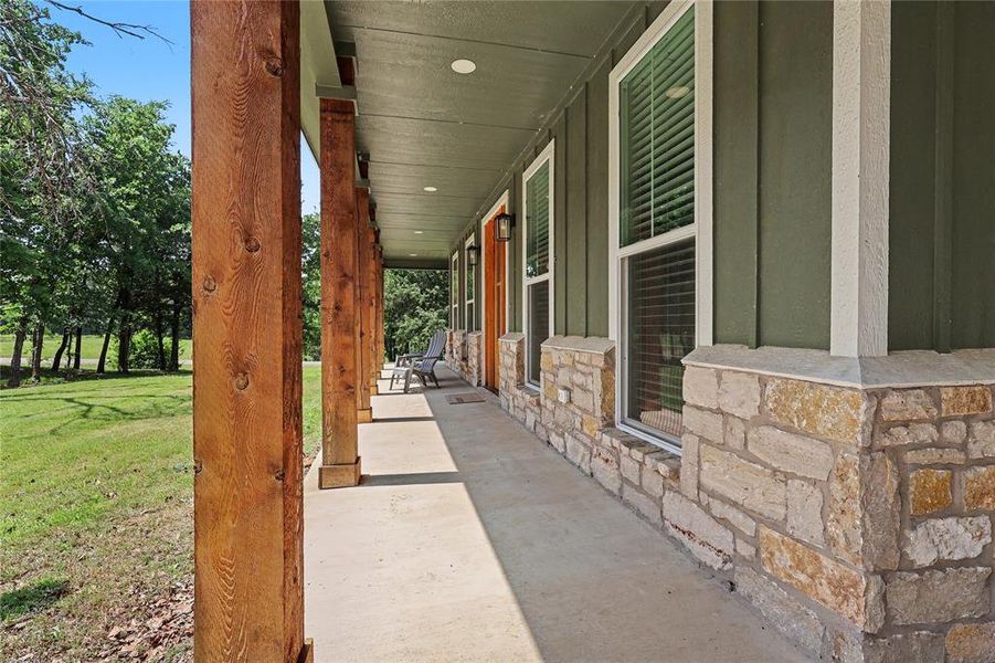 Spacious covered porch with robust wood-finish columns, stone veneer accents, concrete flooring, and a board and batten siding exterior