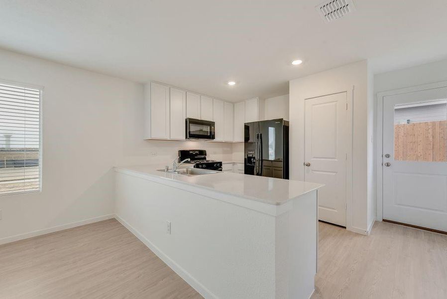 Kitchen featuring light hardwood / wood-style flooring, black appliances, kitchen peninsula, and white cabinets