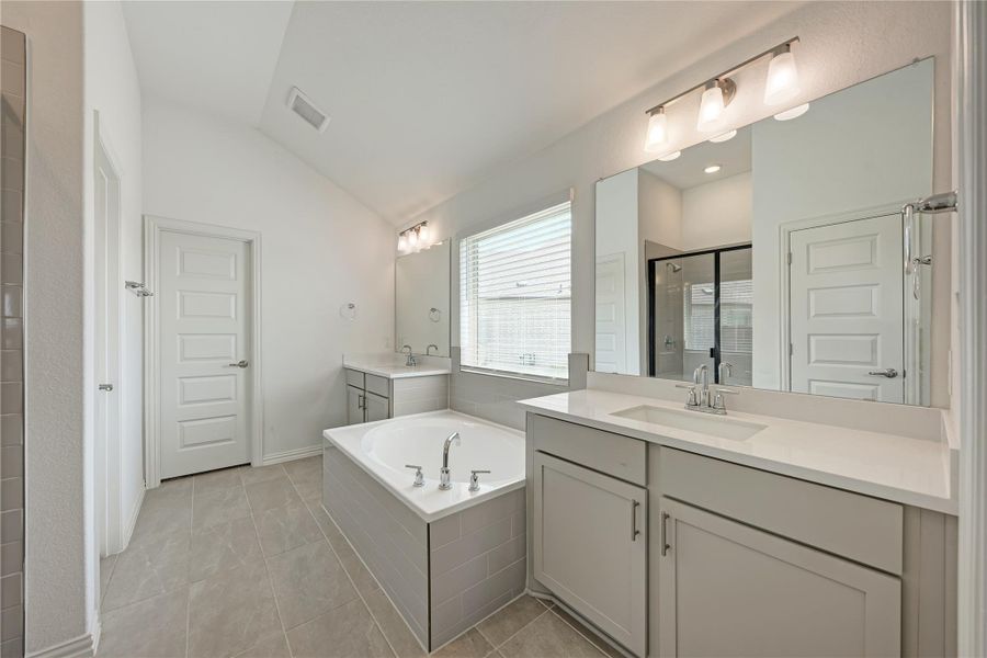A well-lit primary bathroom featuring dual vanities, a separate soaking tub, and a glass-enclosed shower.