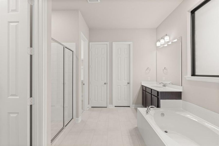 This additional view of your primary bathroom features tile flooring, fresh paint, walk-in shower, a separate garden tub, and a large walk-in closet.