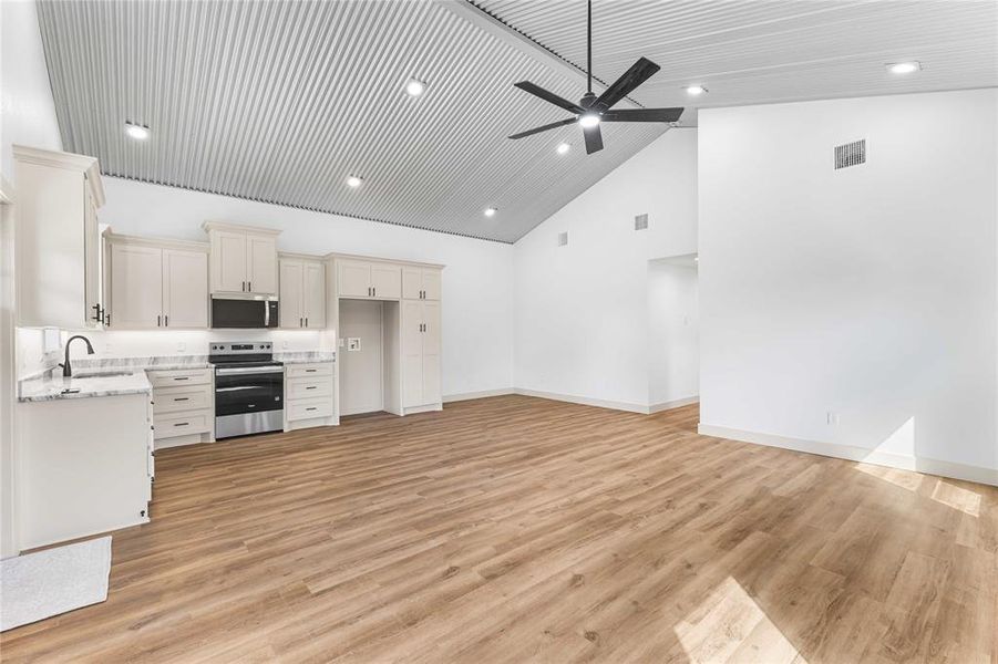 Kitchen featuring stainless steel appliances, light wood-type flooring, high vaulted ceiling, light stone counters, and recessed lighting Kitchen featuring stainless steel appliances, light wood-type flooring, high vaulted ceiling, light stone counters, and recessed lighting