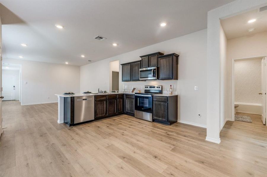 Kitchen featuring appliances with stainless steel finishes, a peninsula, dark brown cabinets, light wood-type flooring, and recessed lighting Kitchen featuring appliances with stainless steel finishes, a peninsula, dark brown cabinets, light wood-type flooring, and recessed lighting