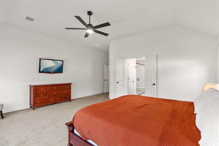 Carpeted bedroom with ceiling fan, lofted ceiling, and ensuite bathroom