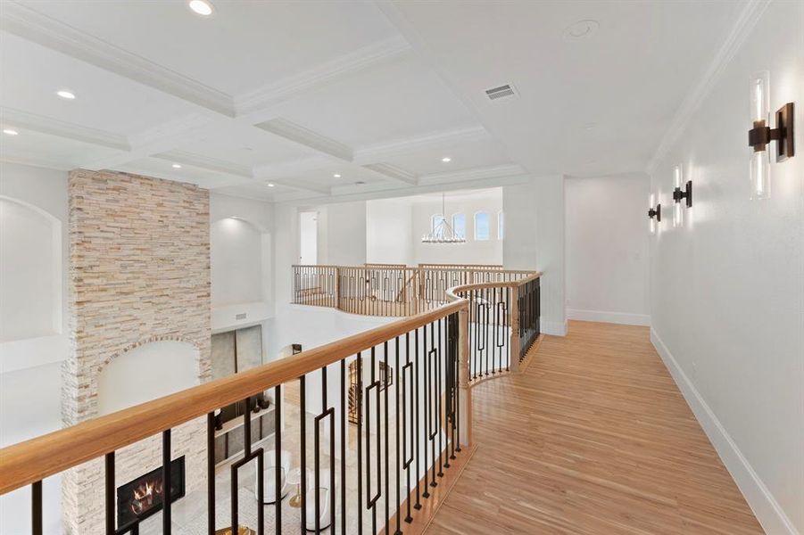 This is a spacious, well-lit upper-level interior space with hard flooring throughout..absolutely no carpet!! This gives you a closer look at the ceiling work. Notice the wall sconces and the open balustrade with metal railings, overlooking a lower level, creating an open and airy feel.