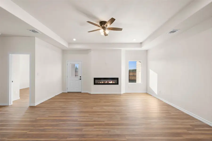 Unfurnished living room featuring a glass covered fireplace, wood finished floors, a tray ceiling, recessed lighting, and a ceiling fan Unfurnished living room featuring a glass covered fireplace, wood finished floors, a tray ceiling, recessed lighting, and a ceiling fan