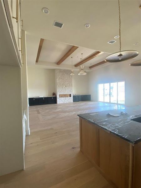 Kitchen featuring dark stone counters, beamed ceiling, a fireplace, light hardwood / wood-style flooring, and decorative light fixtures