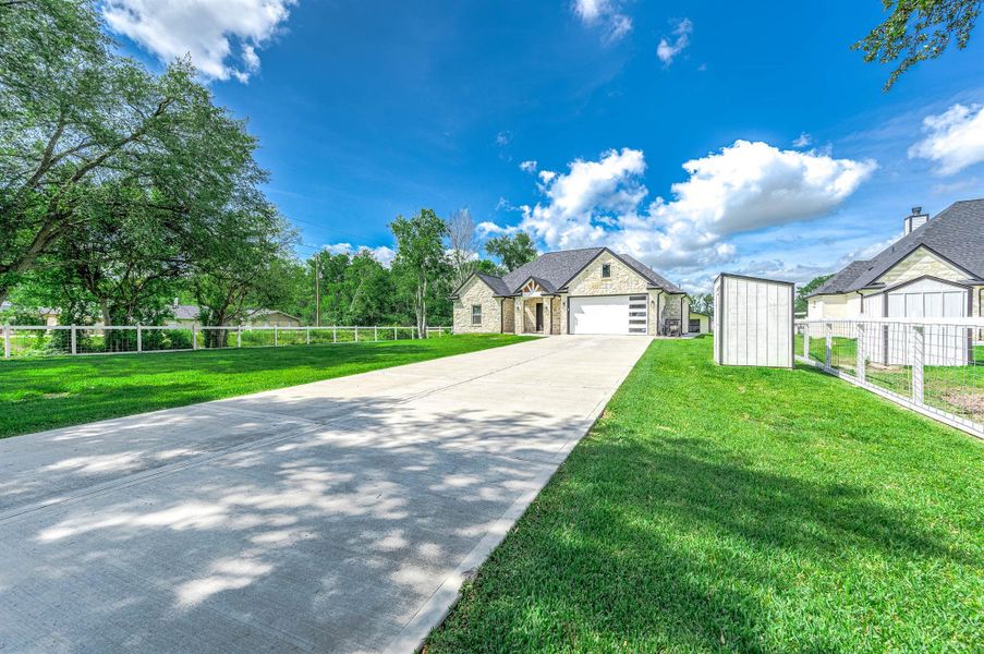 A different angle of the front of the home showcasing the spacious driveway leading to the attached two-car garage. Surrounded by a lush green lawn and mature trees, this property offers a peaceful setting with the perfect blend of modern design and country charm on a beautiful 1-acre tract.