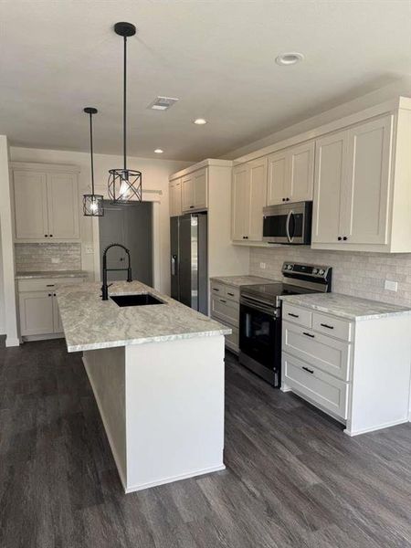 Kitchen featuring tasteful backsplash, appliances with stainless steel finishes, a center island with sink, light stone counters, and dark wood-type flooring Kitchen featuring tasteful backsplash, appliances with stainless steel finishes, a center island with sink, light stone counters, and dark wood-type flooring