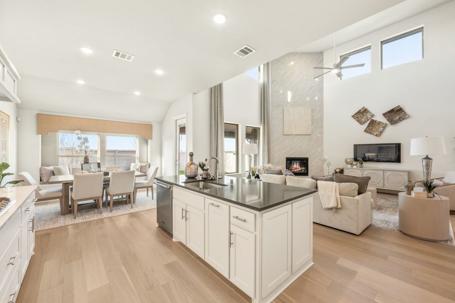 Open-concept kitchen with white island, dark countertops, and adjoining living and dining areas with high ceilings and hardwood floors