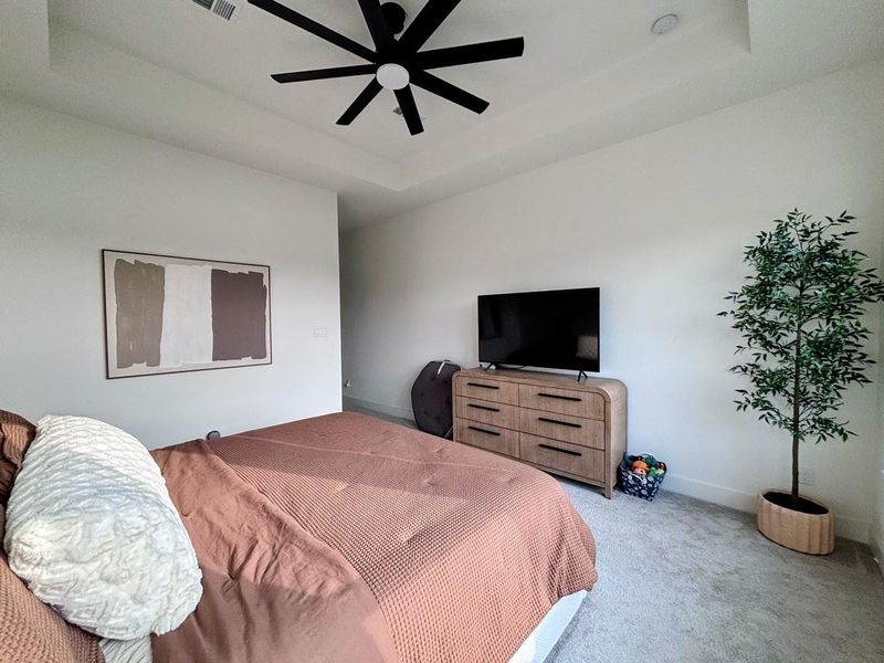 The master bedroom is spacious and bright, with a contemporary design. It has a ceiling fan, multiple windows offering natural light and a view, and is complemented by neutral tones and modern furnishings