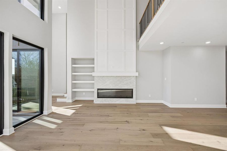 Unfurnished living room featuring a high ceiling, light wood-style floors, a fireplace, recessed lighting, and built in shelves Unfurnished living room featuring a high ceiling, light wood-style floors, a fireplace, recessed lighting, and built in shelves