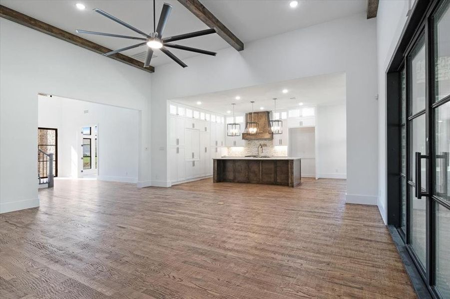 Unfurnished living room with a towering ceiling, ceiling fan, wood-type flooring, sink, and beamed ceiling