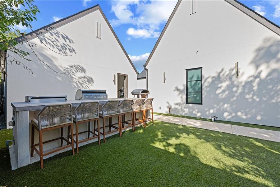View of green turf lawn with an outdoor kitchen and a patio