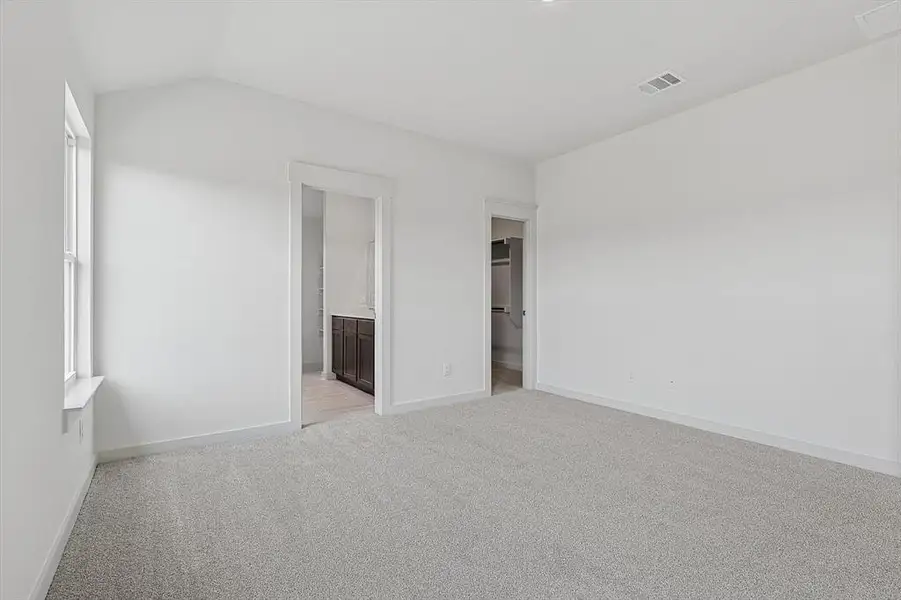 Unfurnished bedroom with a walk in closet, light carpet, lofted ceiling, and connected bathroom Unfurnished bedroom with a walk in closet, light carpet, lofted ceiling, and connected bathroom