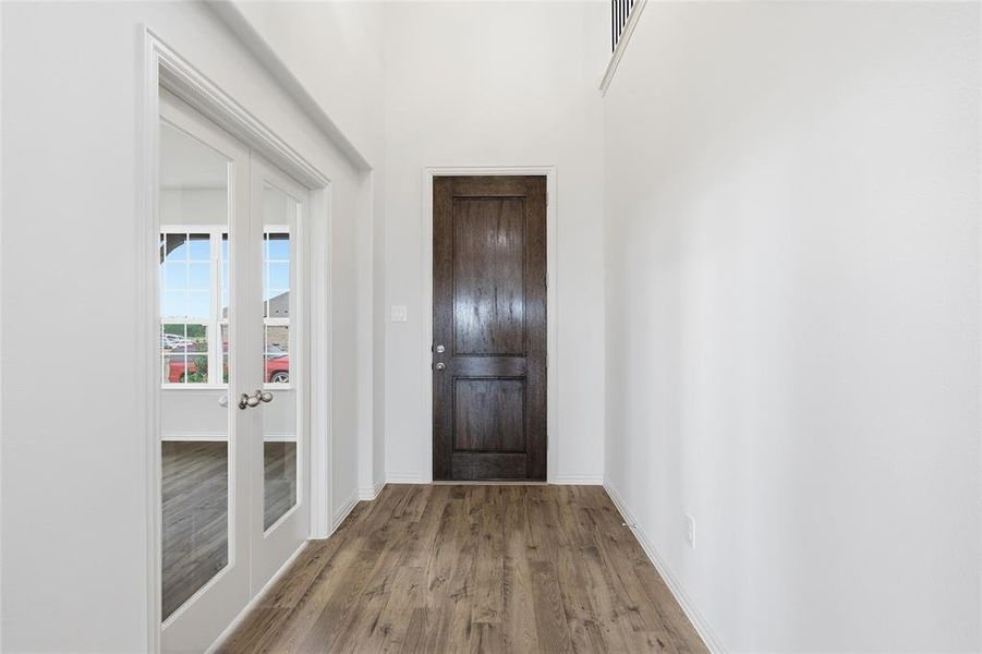 Entryway featuring wood-finish flooring, a dark wood paneled door, and tall white walls