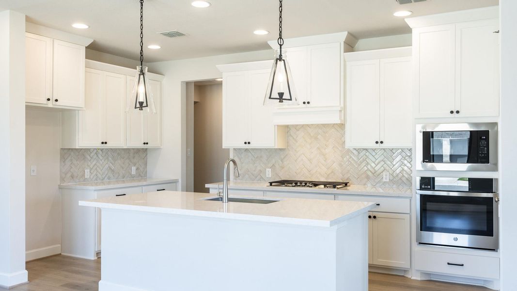 Kitchen with stainless steel appliances, a center island with sink, hanging light fixtures, light stone countertops, and white cabinets
