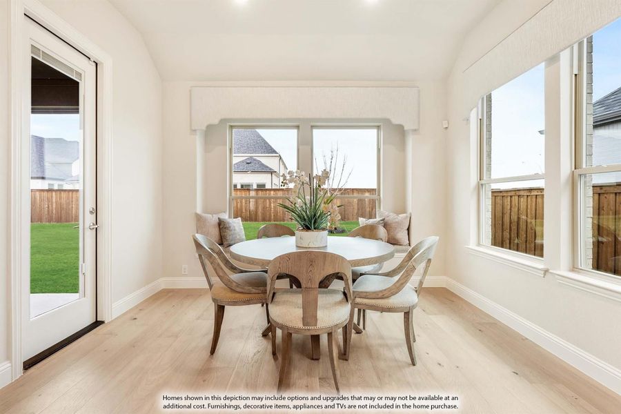Bright breakfast nook with round table, wood chairs, light hardwood floors, and backyard door access.
