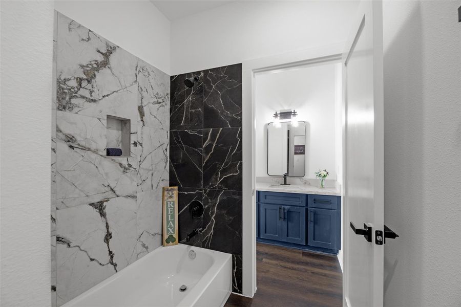 Luxurious bathroom and a stylish bathtub with marble and dark stone tile accents, and a sleek vanity with blue cabinets and a contemporary mirror. Luxurious bathroom and a stylish bathtub with marble and dark stone tile accents, and a sleek vanity with blue cabinets and a contemporary mirror.