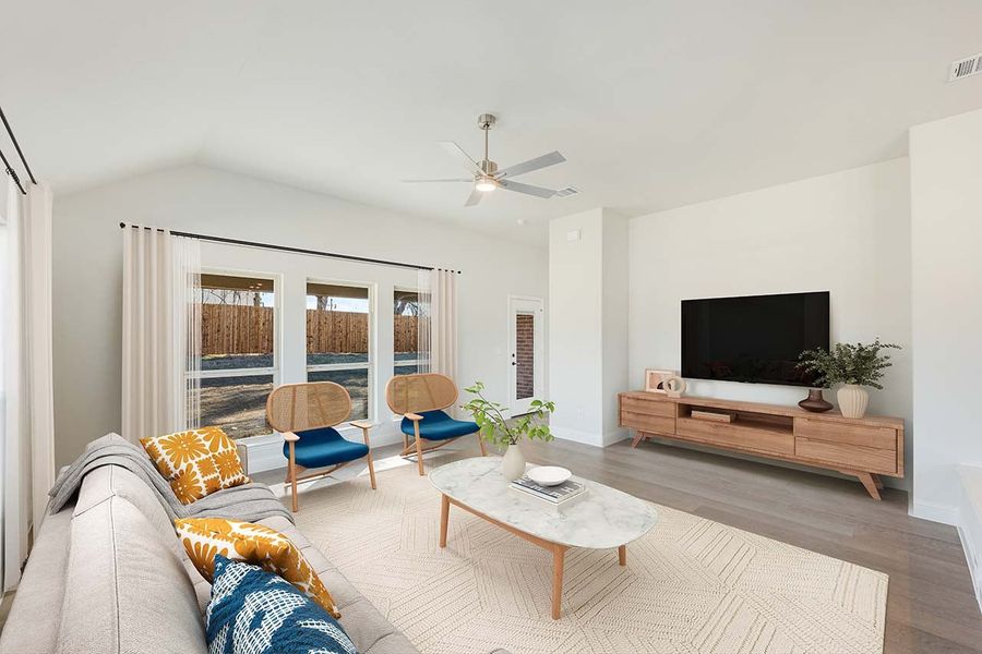 Living room with vaulted ceiling, ceiling fan, wood floors, and large windows overlooking backyard