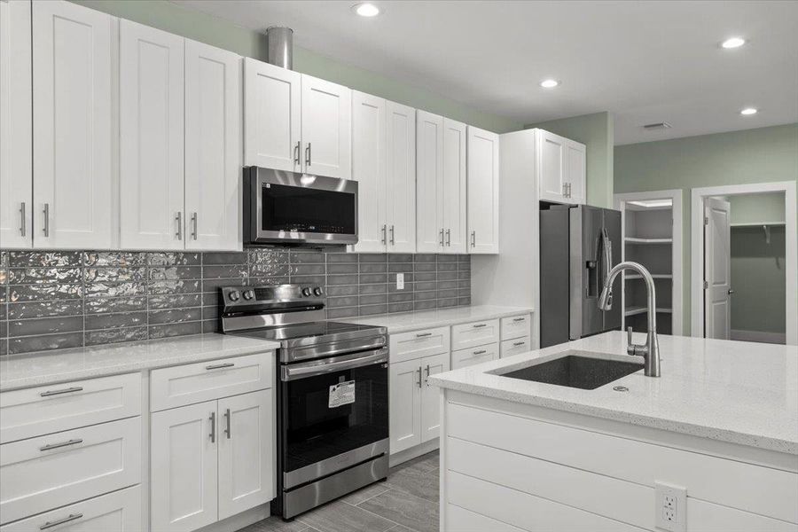 Kitchen featuring stainless steel appliances, white cabinetry, light stone counters, decorative backsplash, and recessed lighting