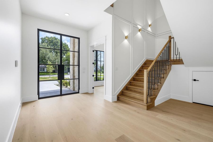 The natural red oak stair case features custom panel work that is complimented by 6 sconces and a grand chandelier.