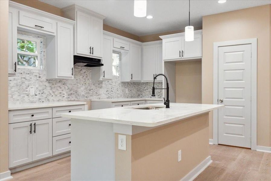 Kitchen with an island with sink, white cabinetry, sink, and decorative light fixtures