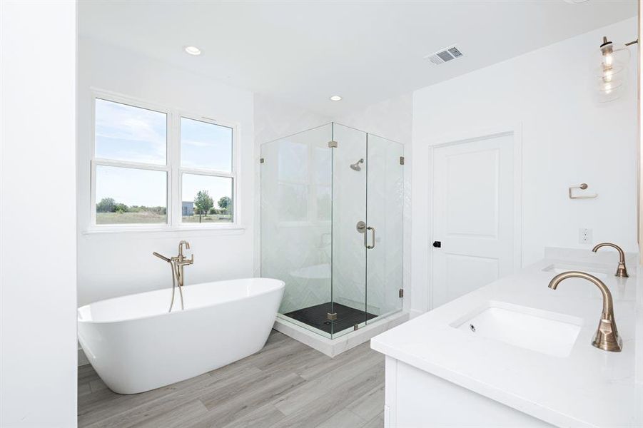 Full bath with a shower stall, a freestanding bath, double vanity, wood finished floors, and recessed lighting