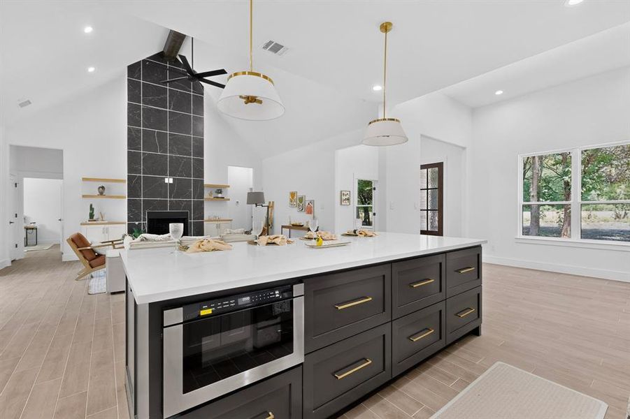 Large kitchen island featuring a white countertop, built-in microwave, and dark cabinetry with gold-toned hardware